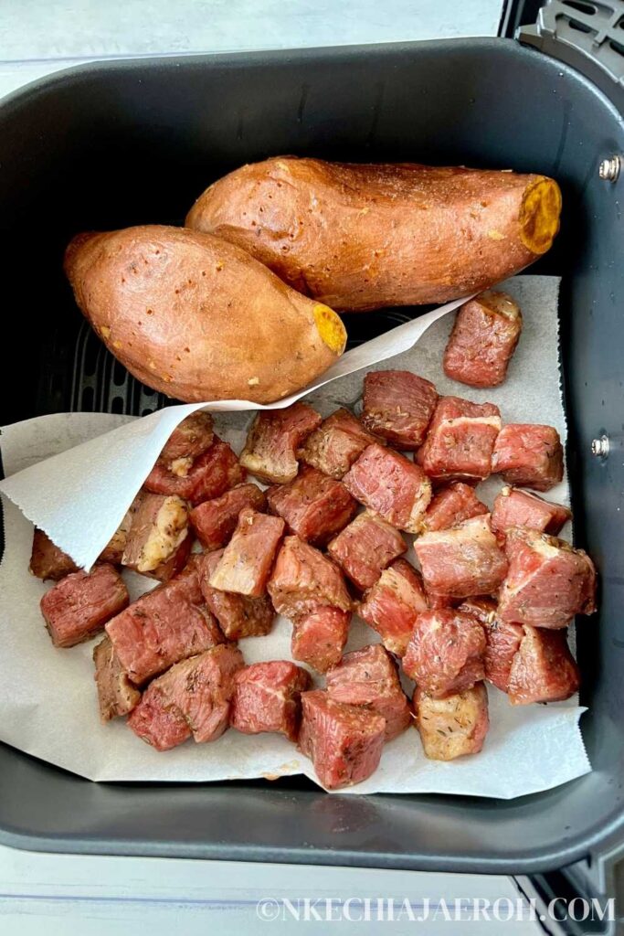 Step five: Add the beef tips; after 15 minutes, add the marinated beef tips into the air fryer. First, move the sweet potatoes to one side of the basket. Then lay a parchment paper and place the meat onto it—Cook for the next 10 minutes. 