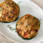 This Healthy Quinoa-Stuffed Acorn Squash is packed with wholesome quinoa, spinach, cranberries, and herbs. A delicious, gluten-free vegetarian main or side dish for your cozy fall meals or Thanksgiving table! Quinoa-stuffed acorn squash halves on a baking tray with fresh herbs. Roasted acorn squash filled with quinoa, cranberries, and spinach. Healthy vegetarian acorn squash stuffed with quinoa and nuts.