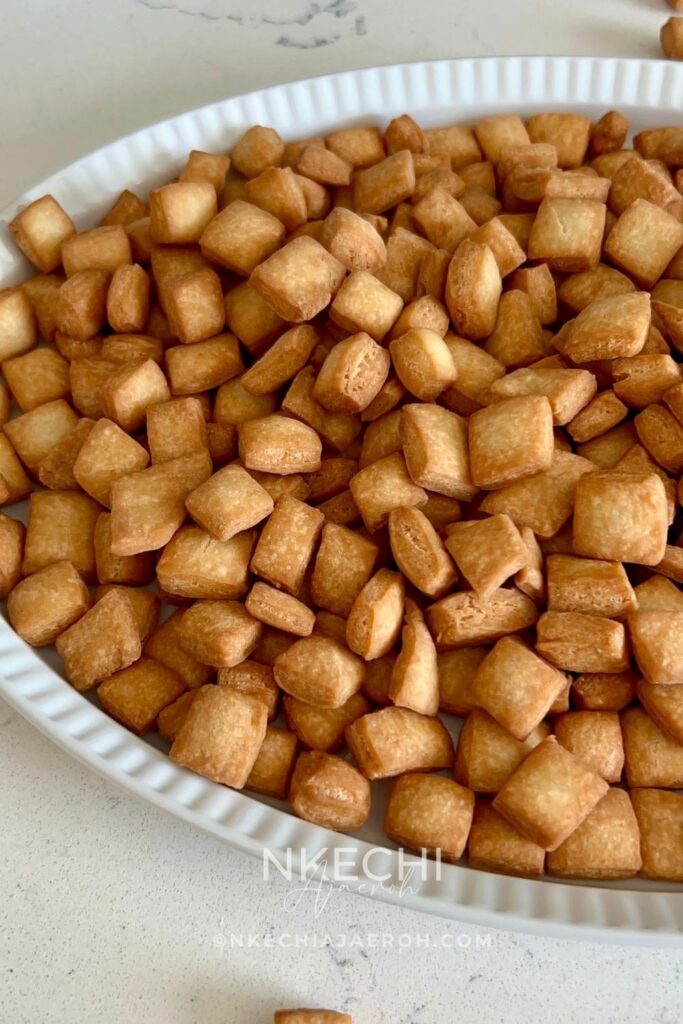 Nigerian chin chin is a popular West African snack known for its crunchy texture, buttery flavor, and lightly sweet taste. Made from a simple dough of flour, butter, sugar, eggs, and nutmeg, chin chin is rolled, cut into small pieces, and fried until golden and crisp. This classic snack is a staple at holidays, birthdays, weddings, and family gatherings, and it’s just as common to find it sold as street food. Chin chin stays crunchy for days and is easy to make in large batches, which makes it perfect for sharing and gifting.
Depending on how long it’s fried, chin chin can range from light golden to deep brown, with each shade offering a satisfying crunch. For many Nigerians and West Africans, chin chin isn’t just a snack — it’s a nostalgic treat that brings back memories of growing up and celebrating together.