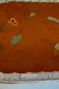 Pour in the coconut milk, Nigerian tomato stew, and chicken broth. Using a spatula, mix thoroughly so the rice is evenly coated. Add the seasoning and herbs.