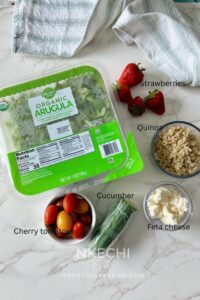 The ingredients for the salmon, strawberry, quinoa, arugula salad include organic arugula, cooked quinoa, strawberries, cucumber, cherry tomatoes, crumbled feta cheese, and Extra Virgin Olive Oil.